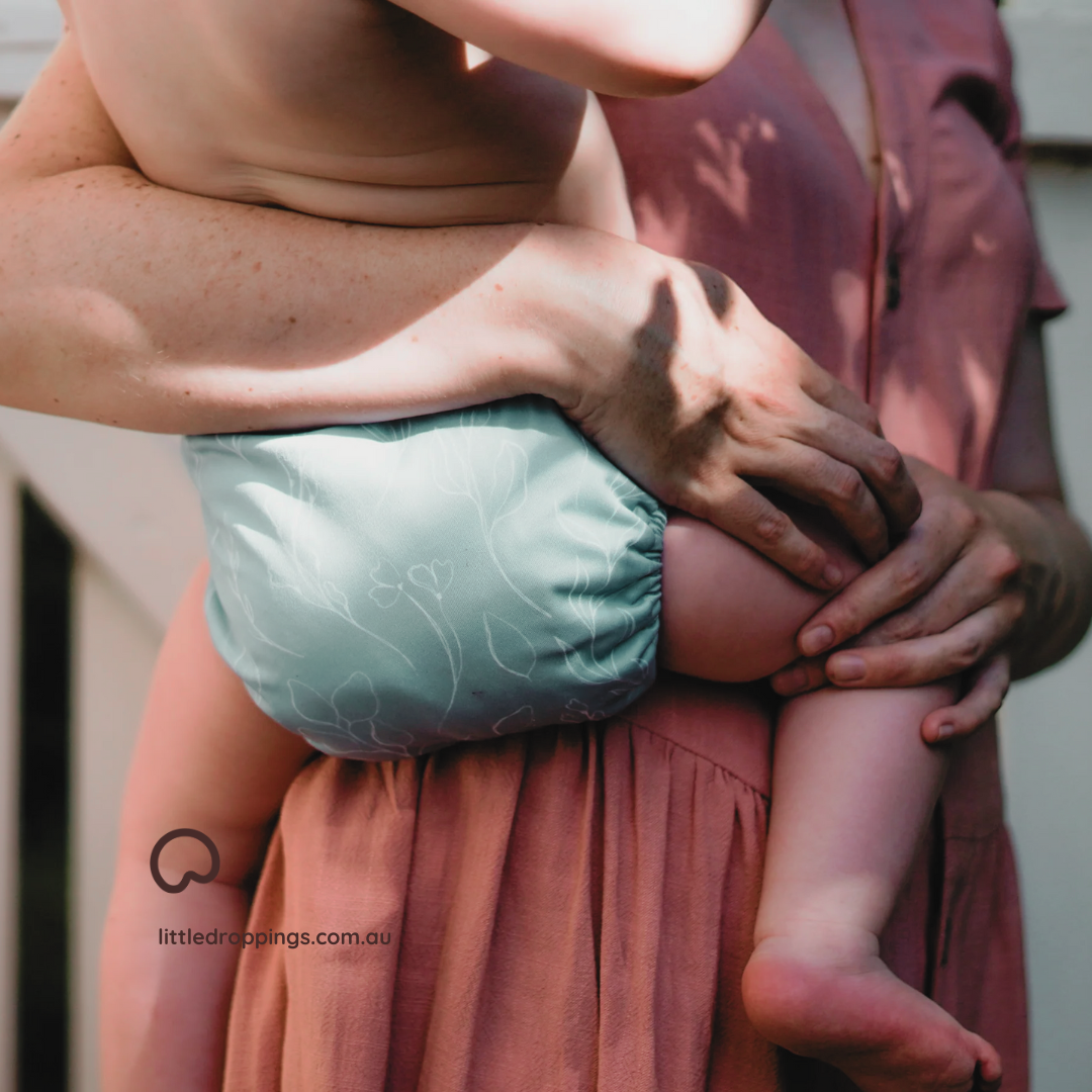 woman holding a baby who is wearing a reusable cloth nappy. 